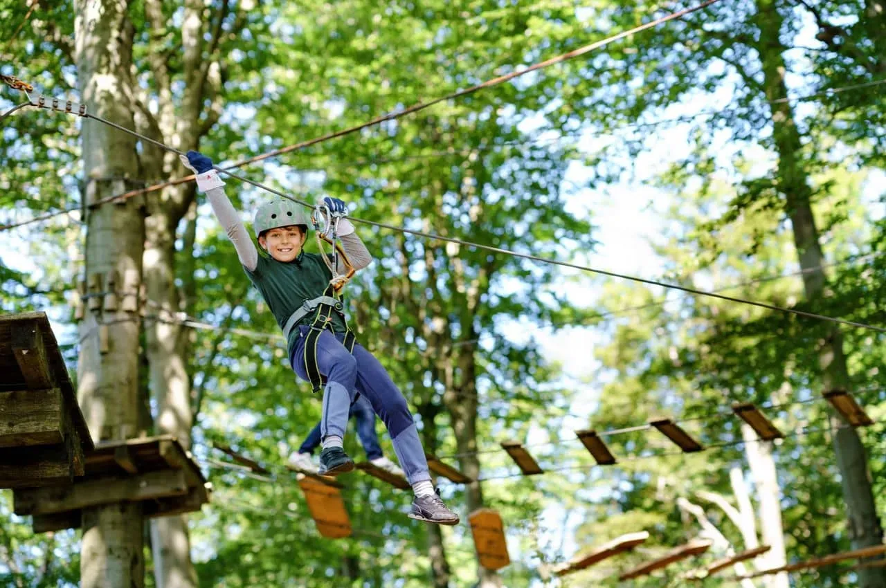 Kind met helm slingert lachend aan zipline tussen de bomen