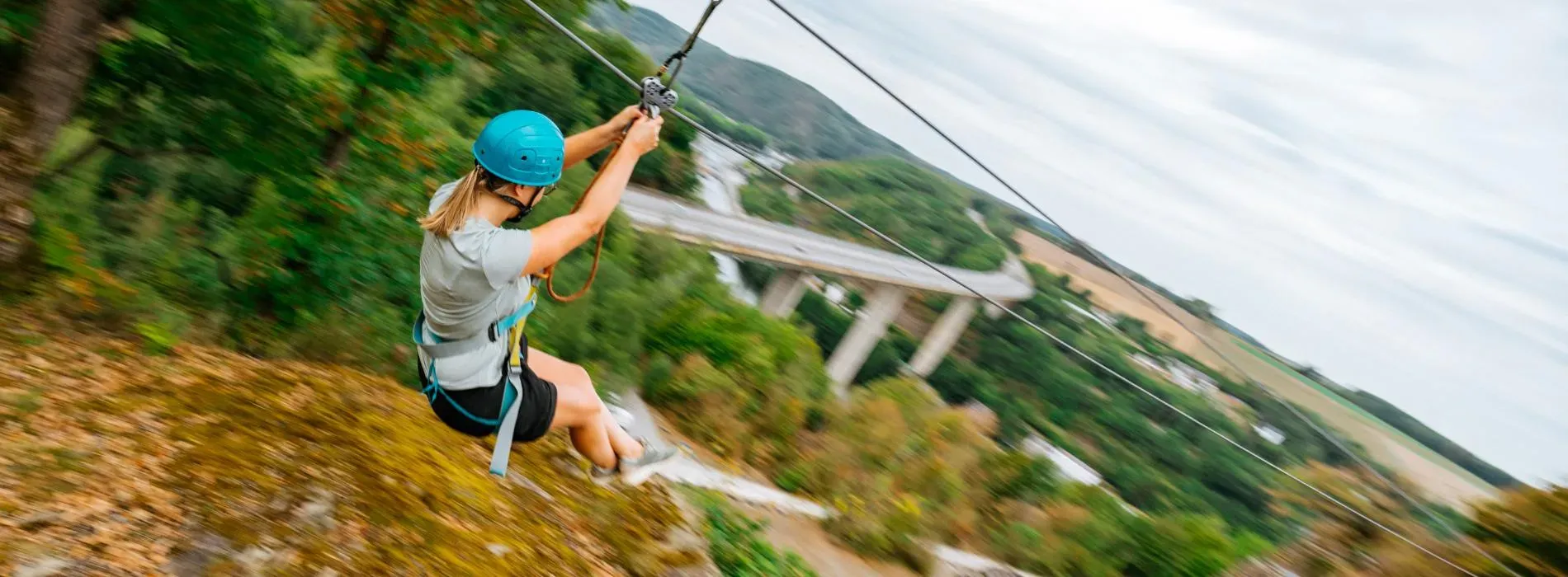 Vrouw met helm glijdt aan zipline boven groene Maasvallei
