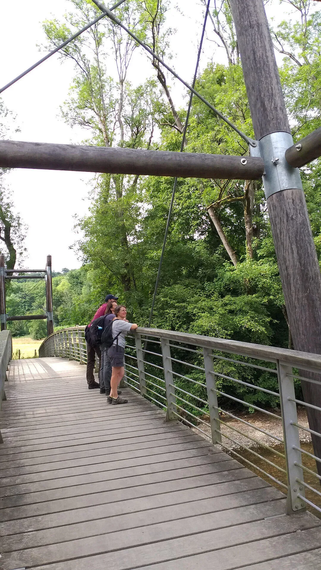 Wandelaars op moderne hangbrug met houten dek boven de Lesse