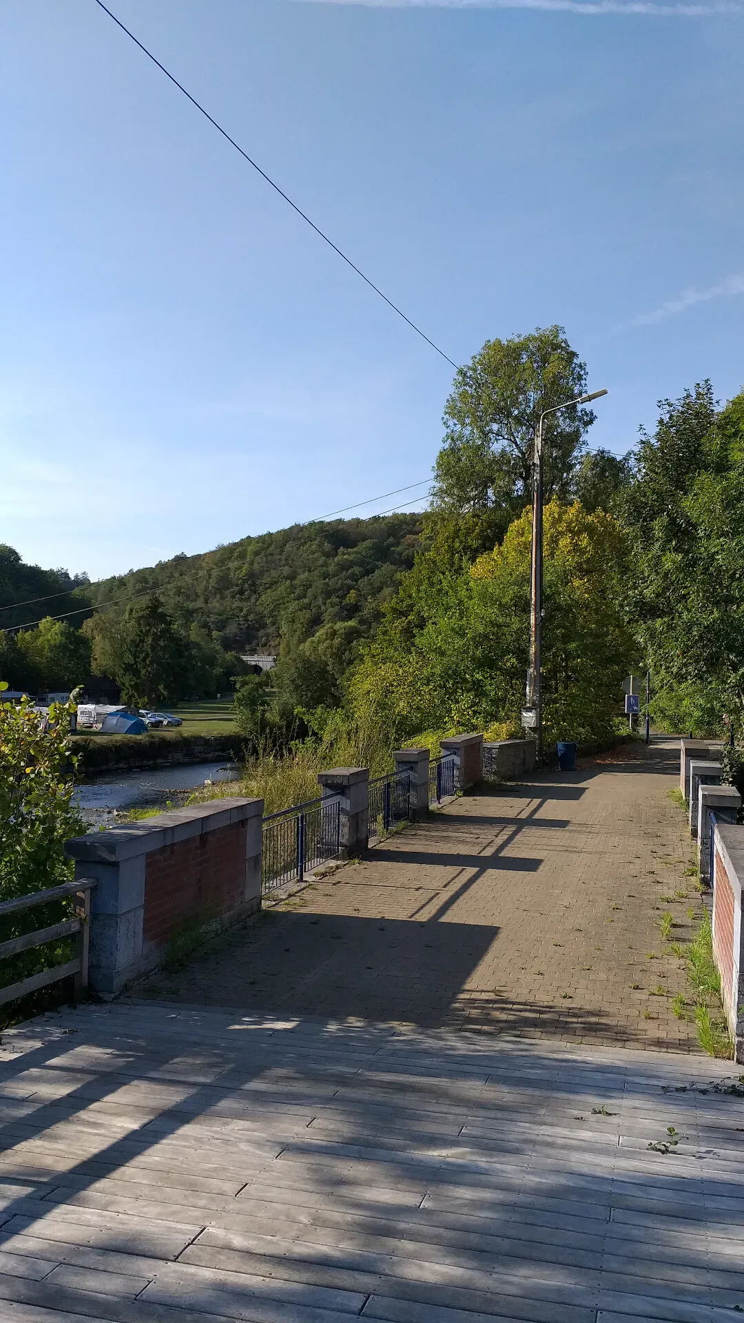 Houten brug over de Lesse met uitzicht op beboste heuvel