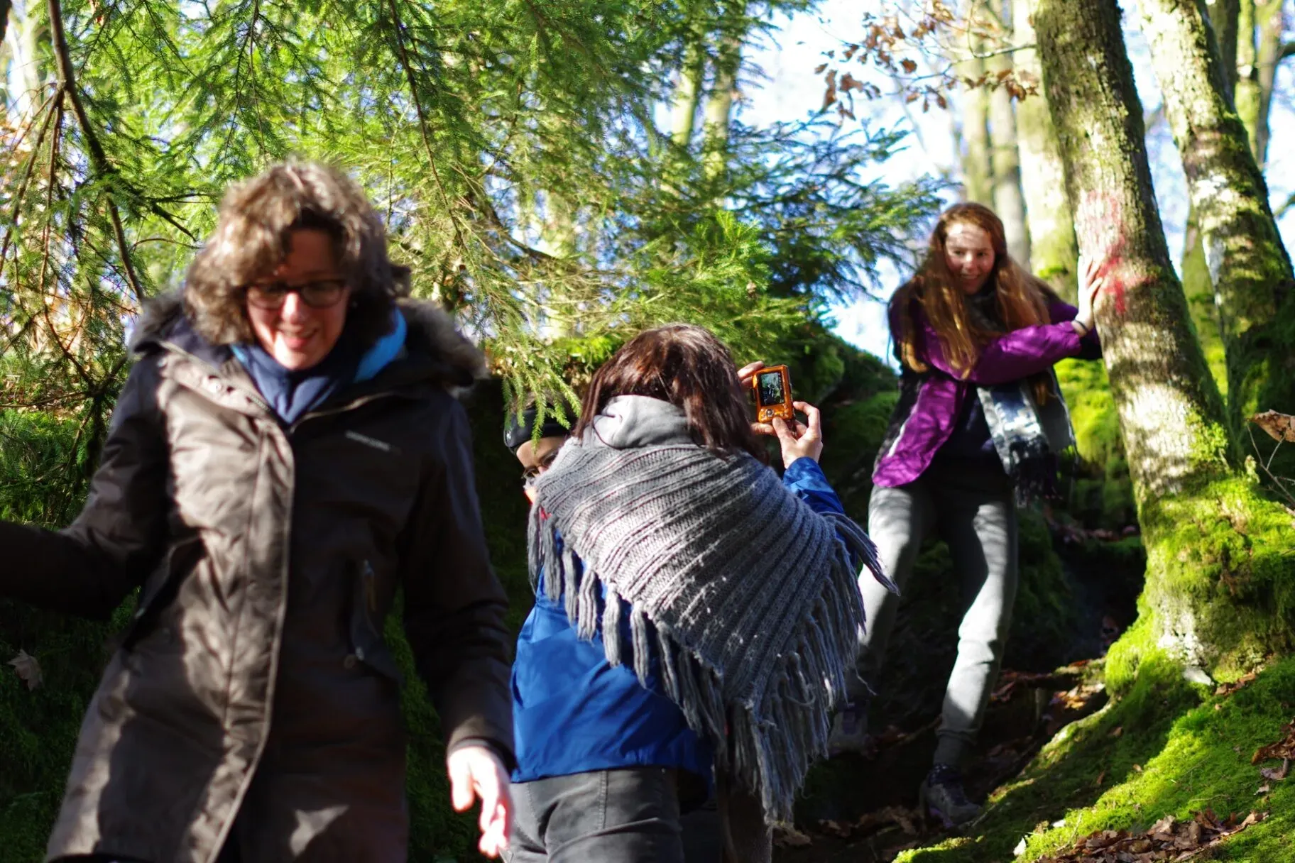 Groep vrouwen wandelt door mosrijk bos, één maakt foto met camera