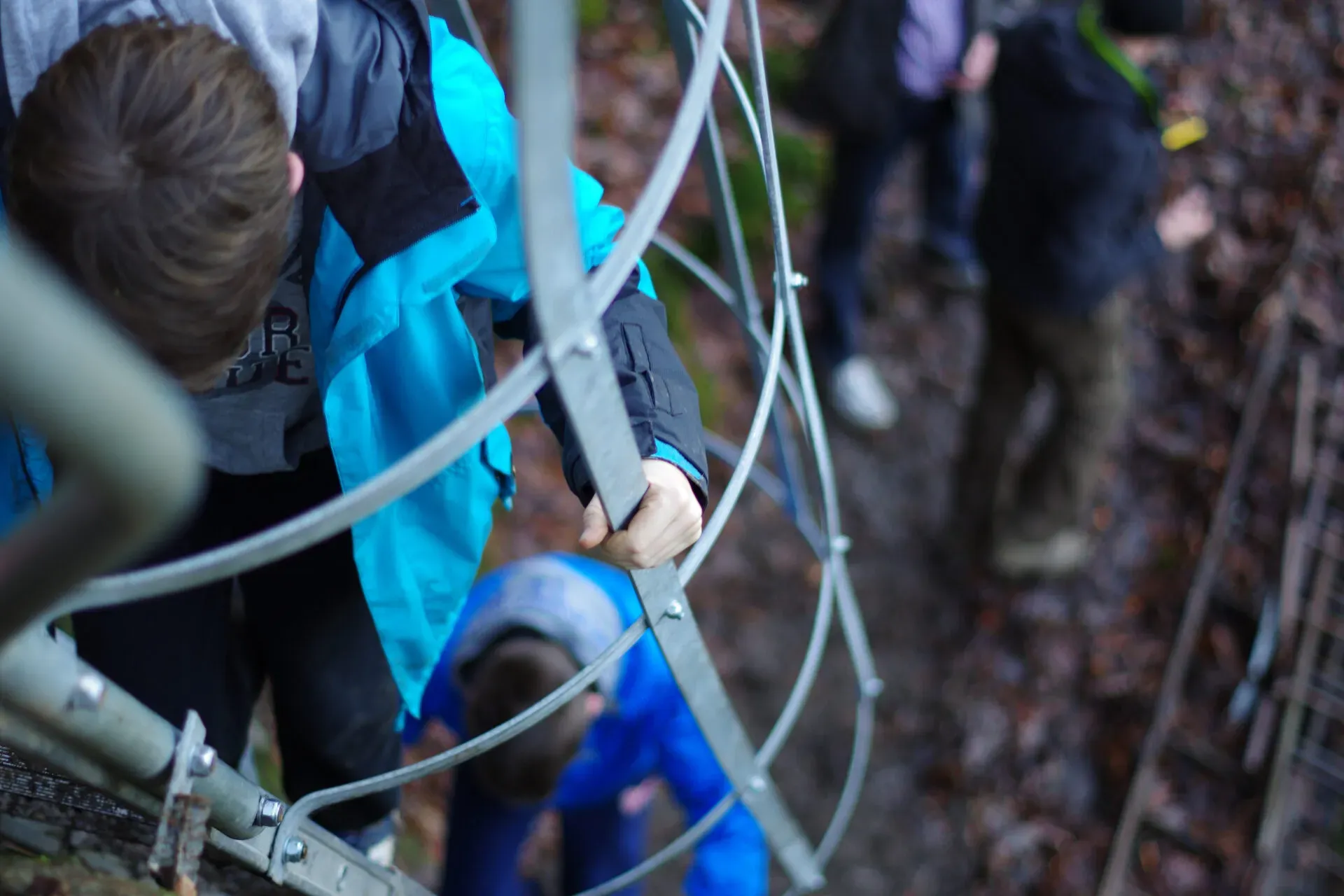 Kinderen klimmen metalen ladder af, gezien van bovenaf door kooi