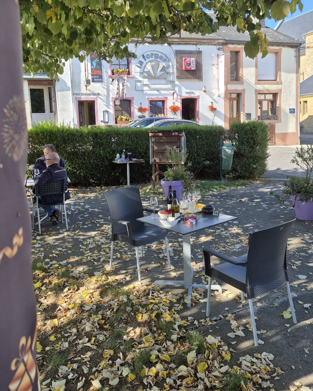The terrace of La Forgerie under the trees on Place du Centenaire in Sainte-Cécile, with the café's façade