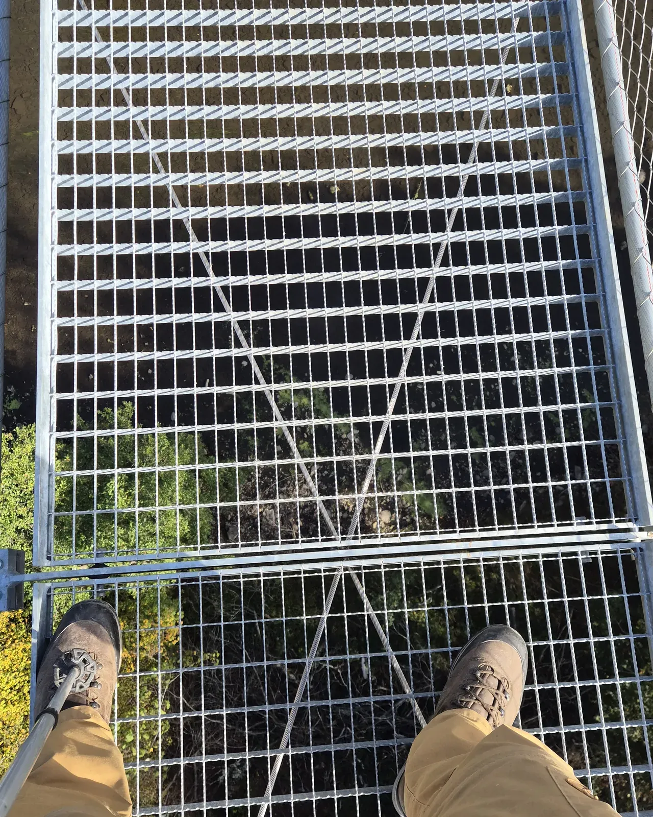 Looking down through the steel grating of the bridge, walking boots and the valley far below